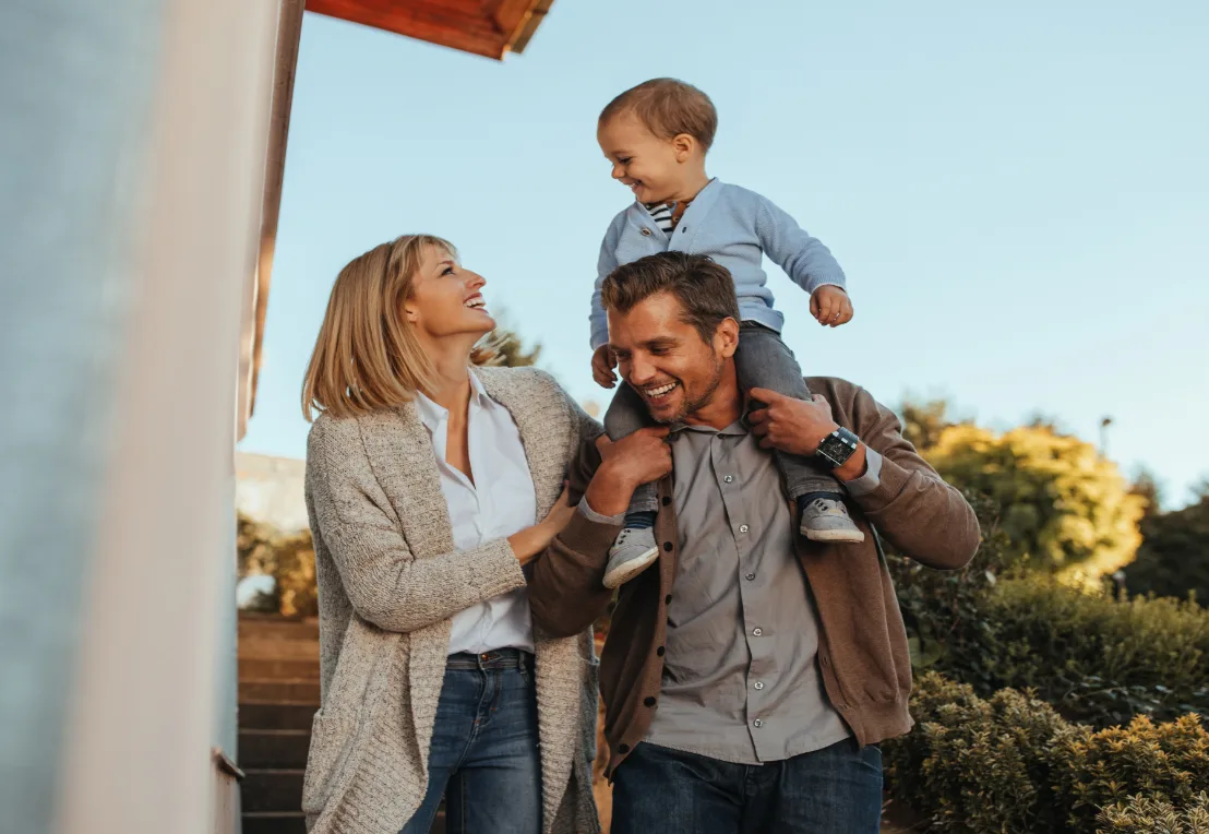 Family smiling outdoors with a child on his father's shoulders